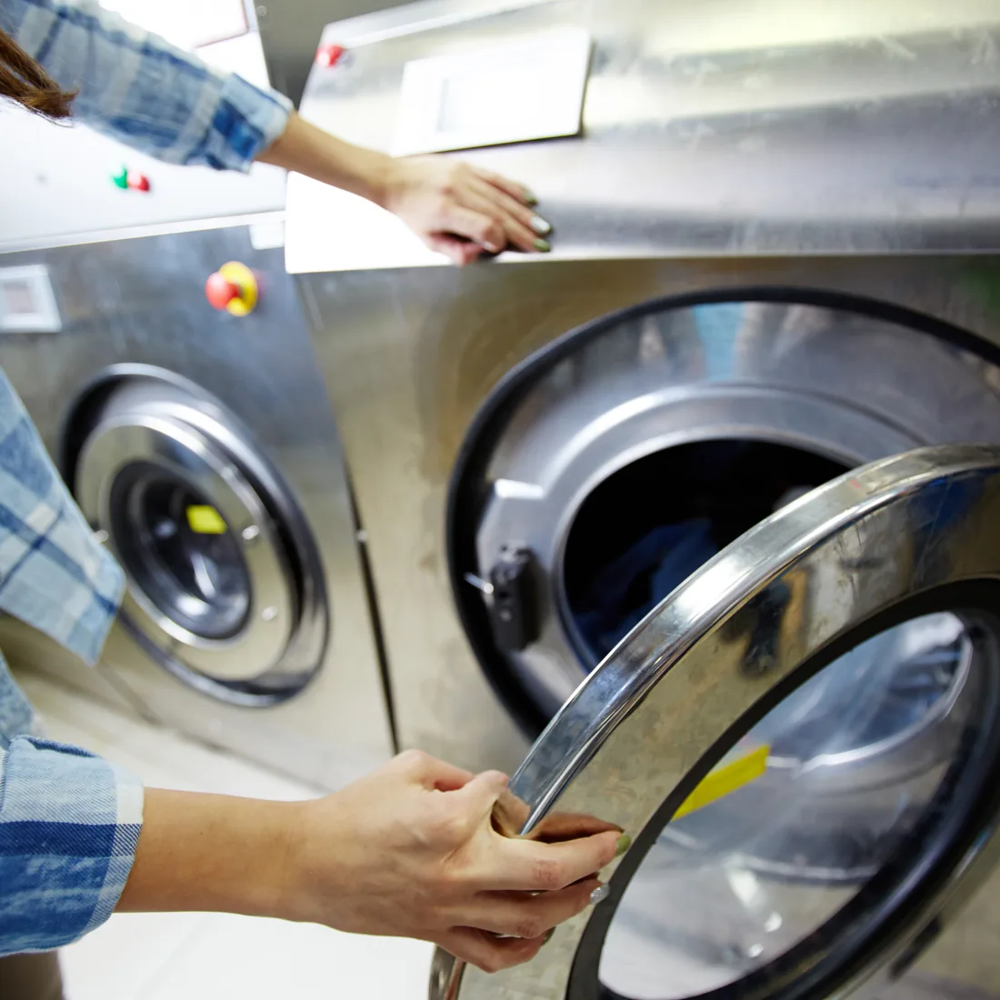 Hands loading laundry into the open door of a large stainless commercial washer