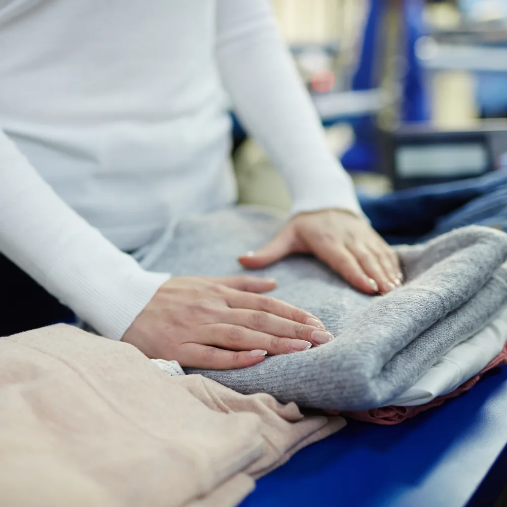 An attendant pressing and folding linen in a commercial laundry