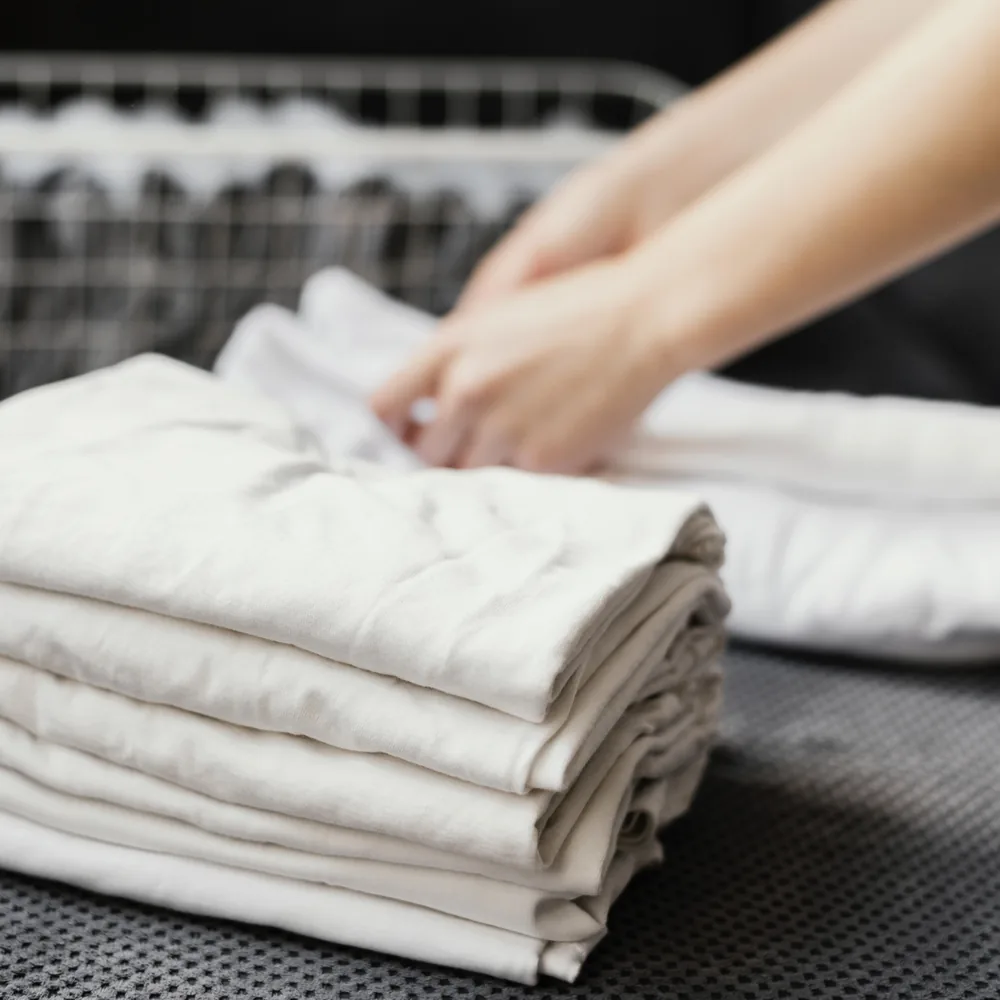 Hands folding clean white laundry into a neat stack
